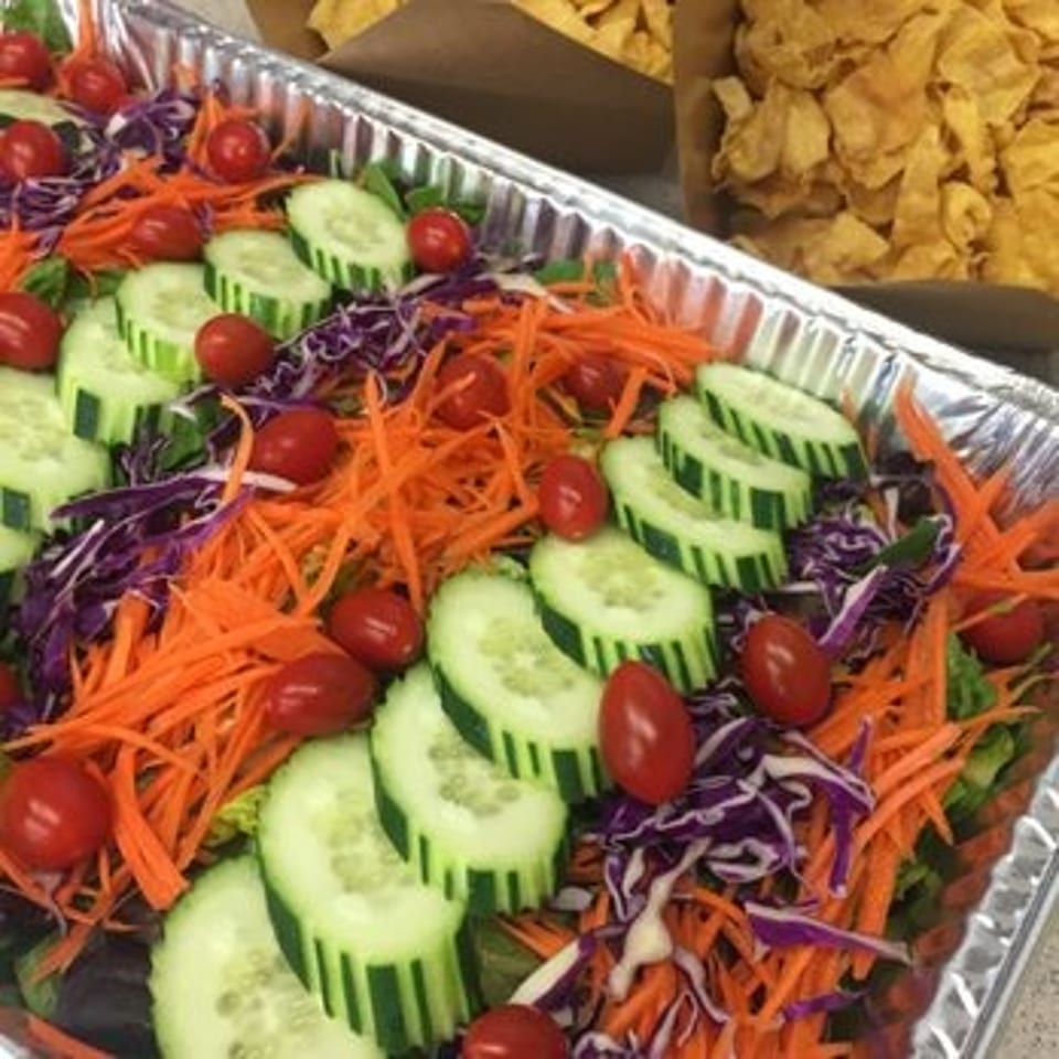 Colorful salad tray with sliced cucumbers, cherry tomatoes, shredded carrots, red cabbage, and tortilla chips.