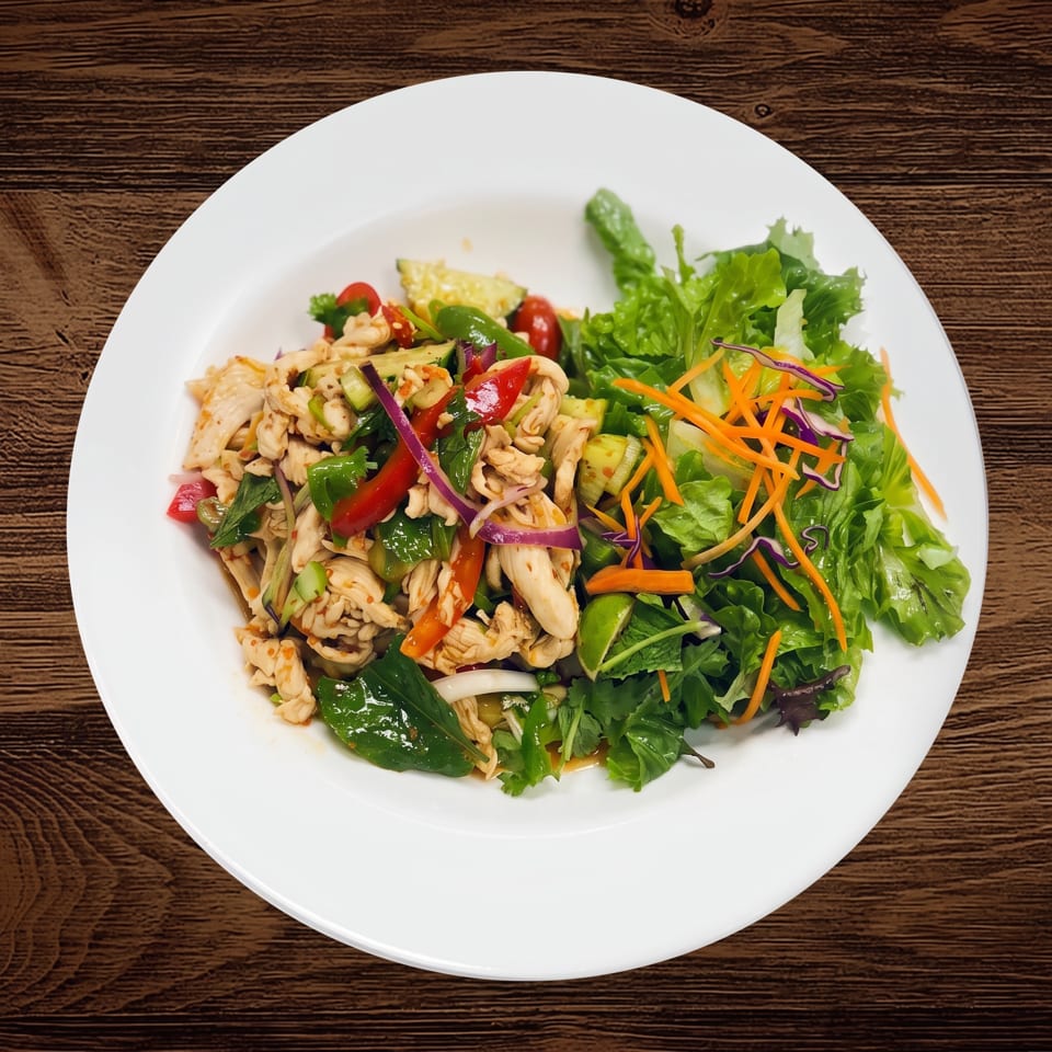 Plate of stir-fried chicken, vegetables, and noodles served alongside fresh leafy salad on a wooden table.