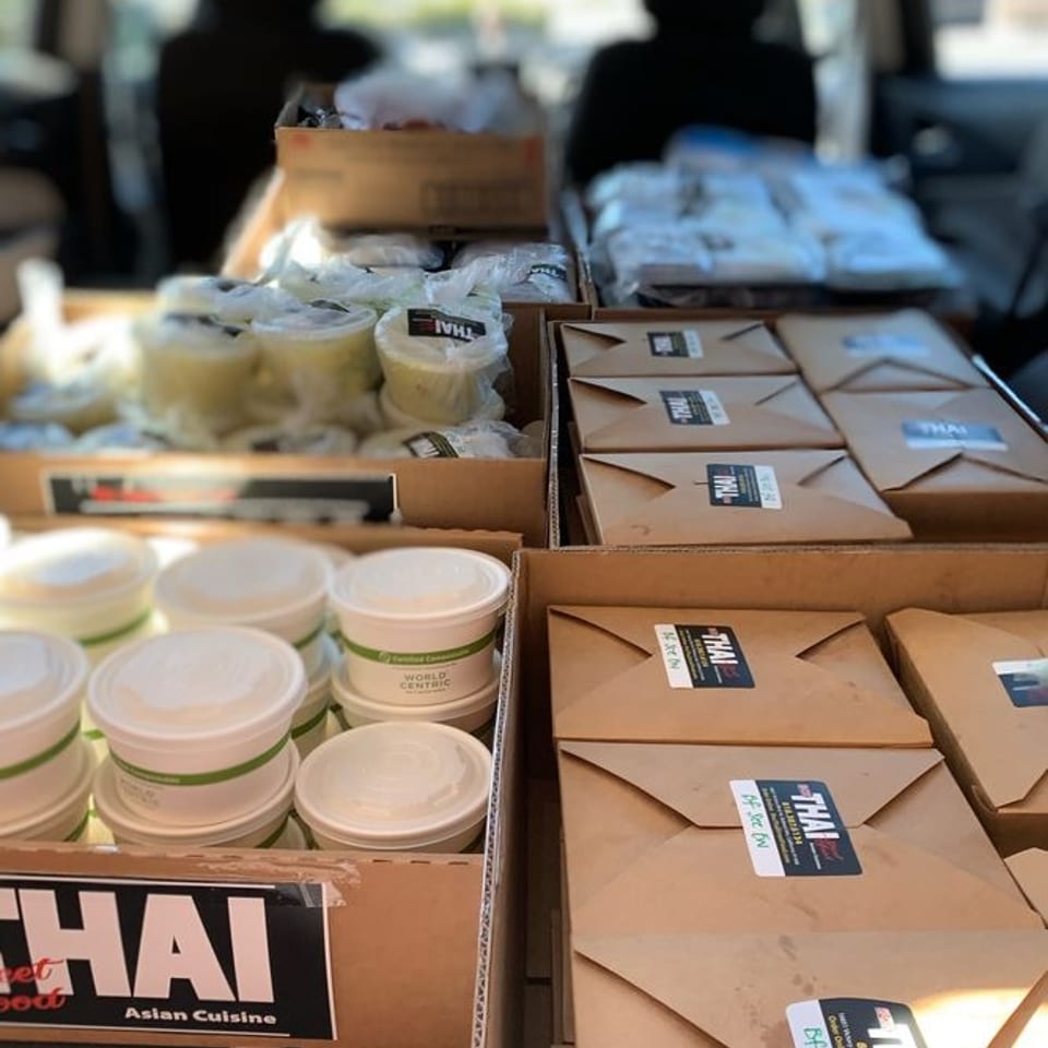 Car trunk filled with boxed Thai Asian cuisine meals and stacked takeaway containers, labeled for delivery.
