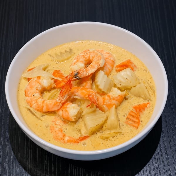 A white bowl filled with creamy yellow shrimp curry, pineapple chunks, and sliced carrots.