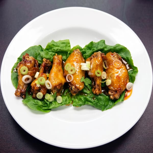 Five glazed chicken wings on a bed of green lettuce, garnished with sliced scallions.