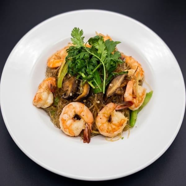Glass noodles with shrimp, mushrooms, and green vegetables, garnished with fresh cilantro on a white plate.