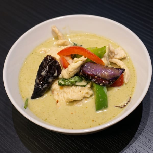Green curry with chicken, red and green bell peppers, and eggplant in a white bowl.