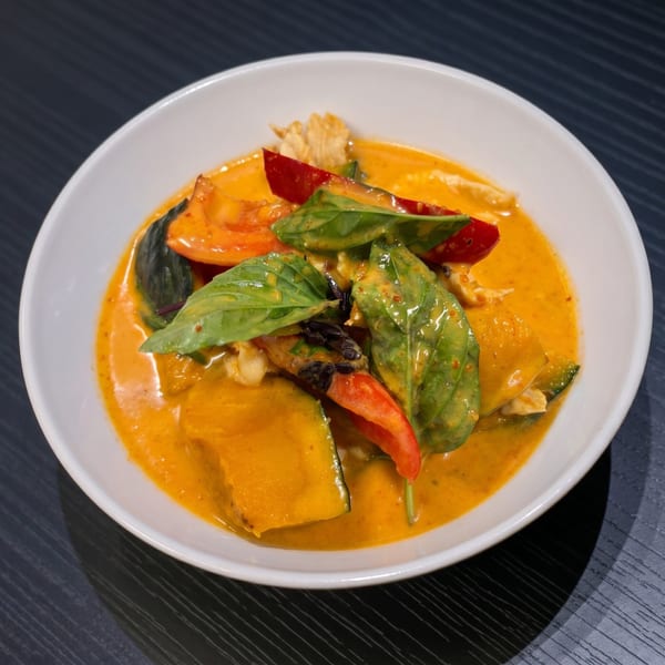 A vibrant orange curry with pumpkin, red bell peppers, and basil leaves in a white bowl.